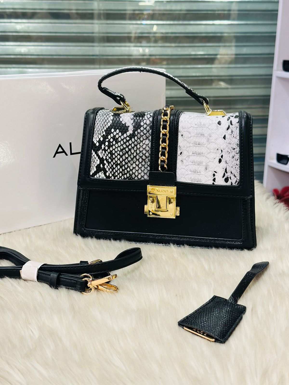 Black handbag with snake print and gold accents on a white surface