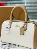 Coach handbag with beige handle and white body on a reflective surface