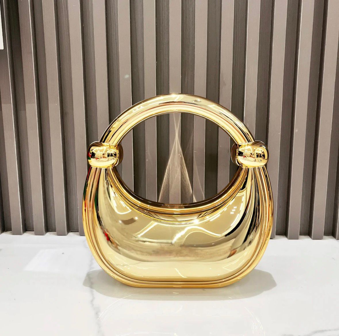 Gold handbag with circular handle against a striped curtain background
