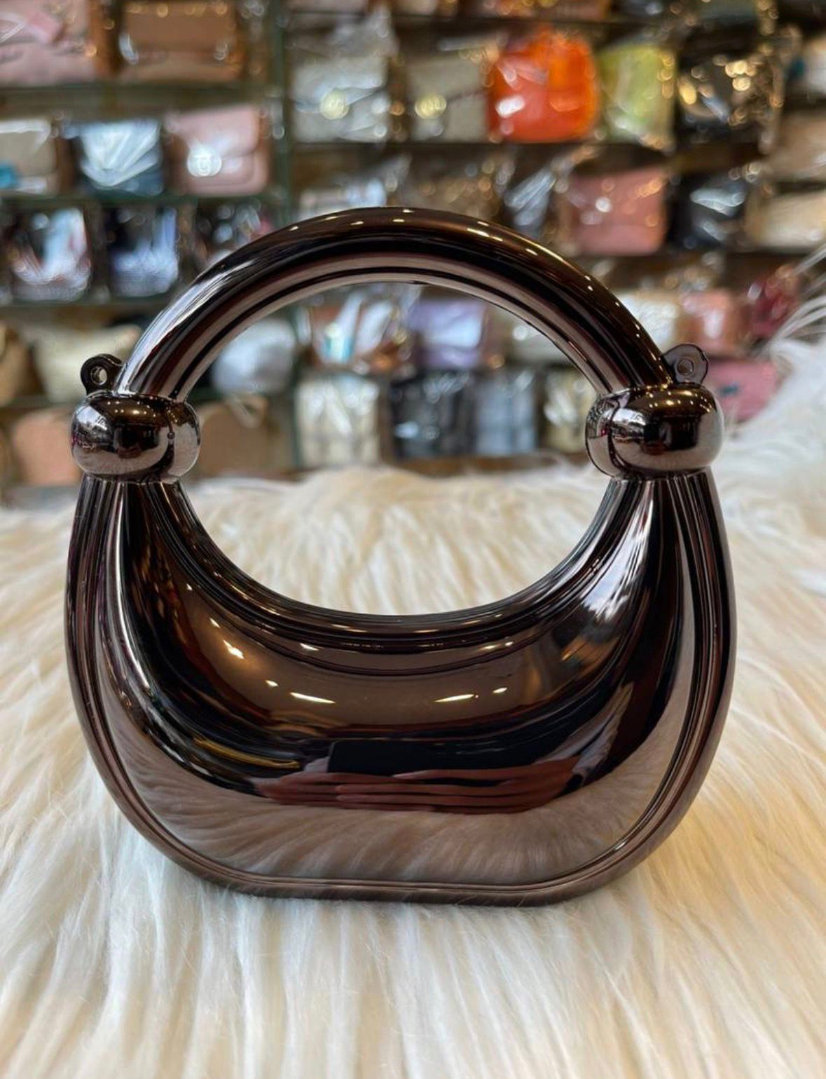 Black handbag with a reflective surface on a textured white surface.