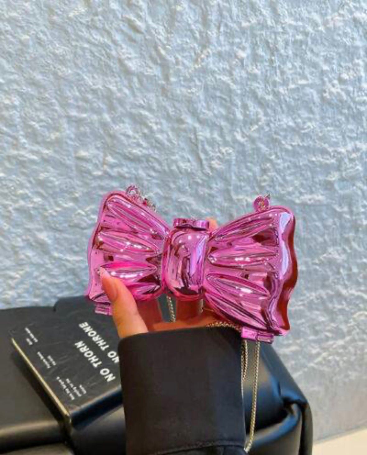 Pink bow-shaped handbag held by a person against a textured wall.