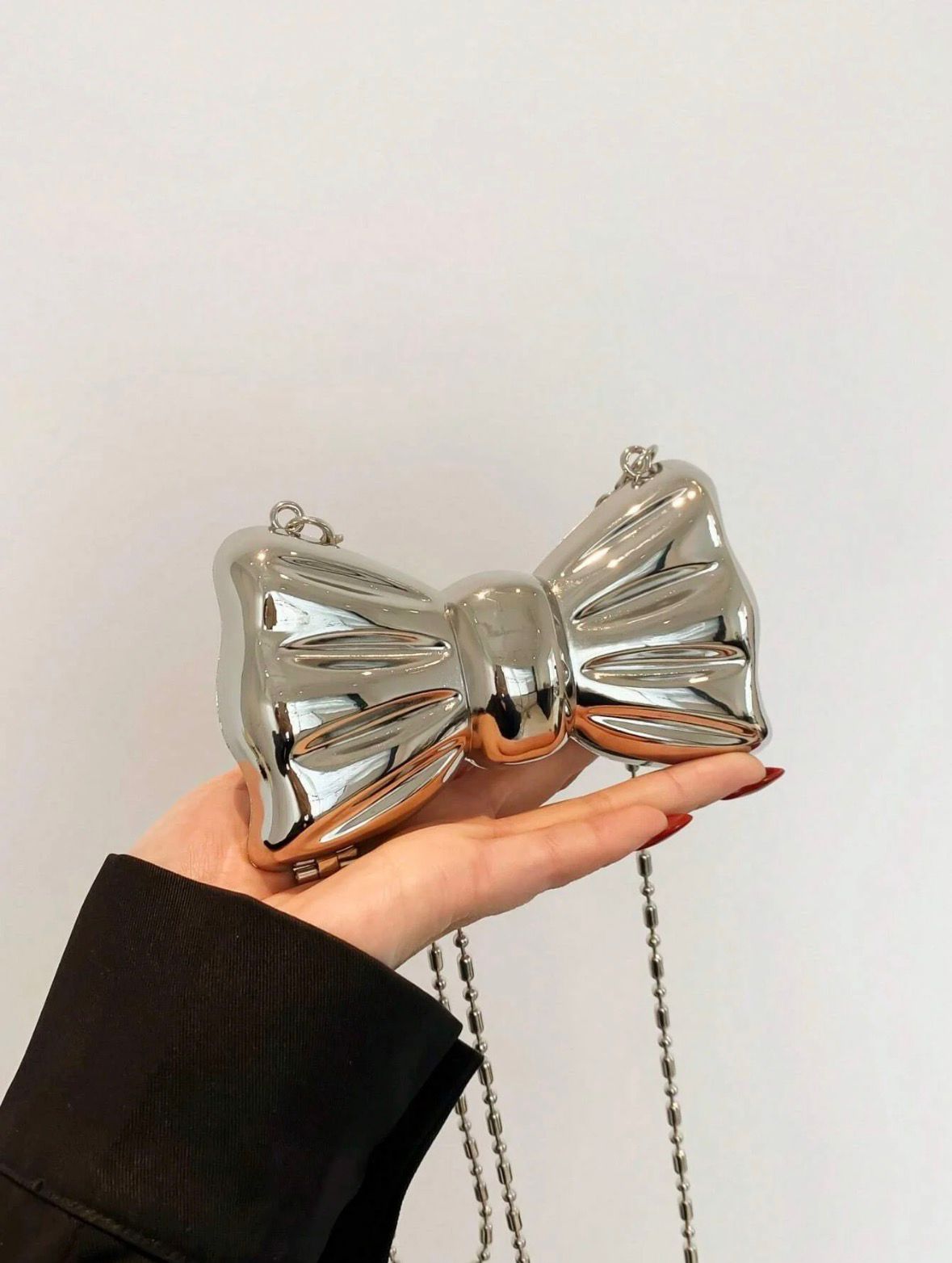 Metallic bow-shaped handbag held by a hand against a plain background