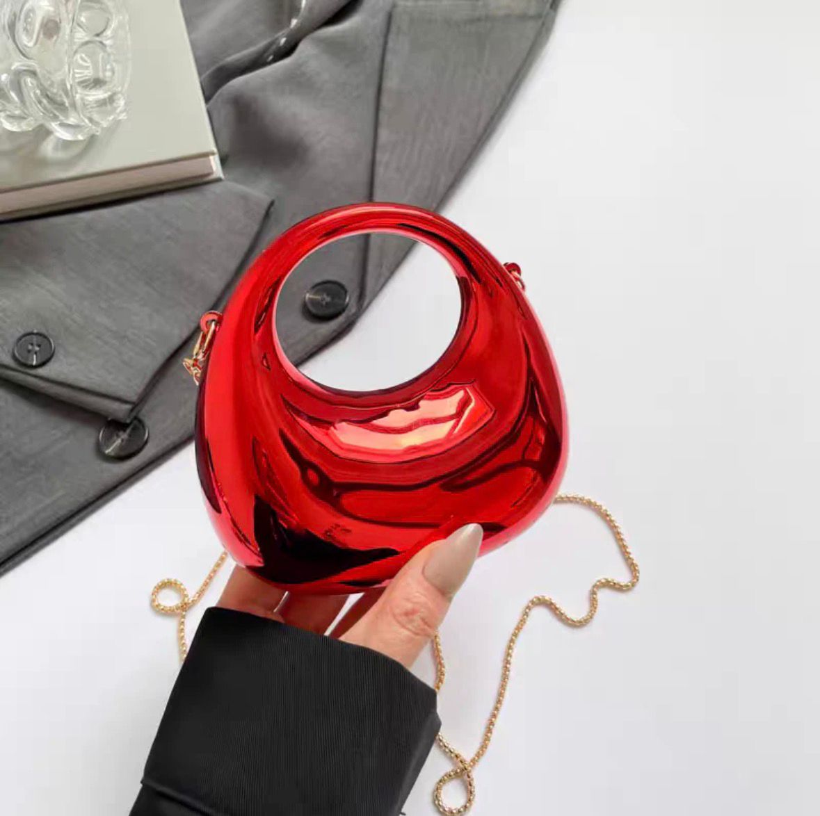 Red handbag with a gold chain held by a hand on a white background