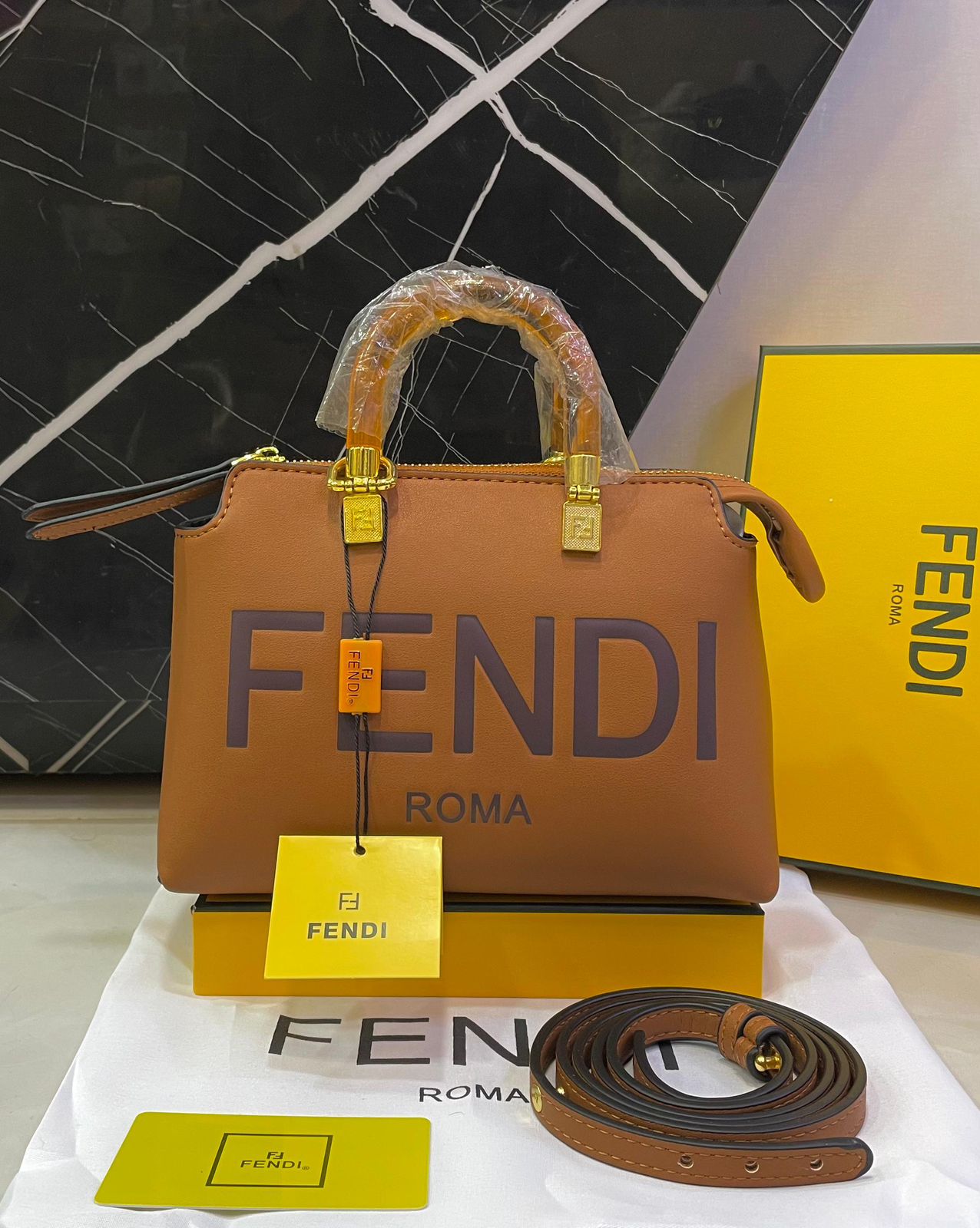 Brown Fendi handbag with gold hardware on a white surface with a black and white patterned background.