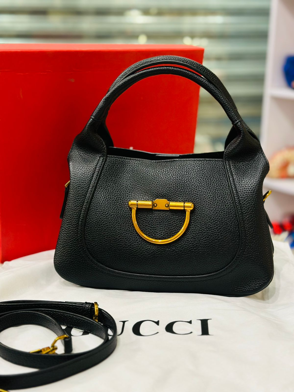 Black handbag with gold hardware on a white surface, with a red box in the background.