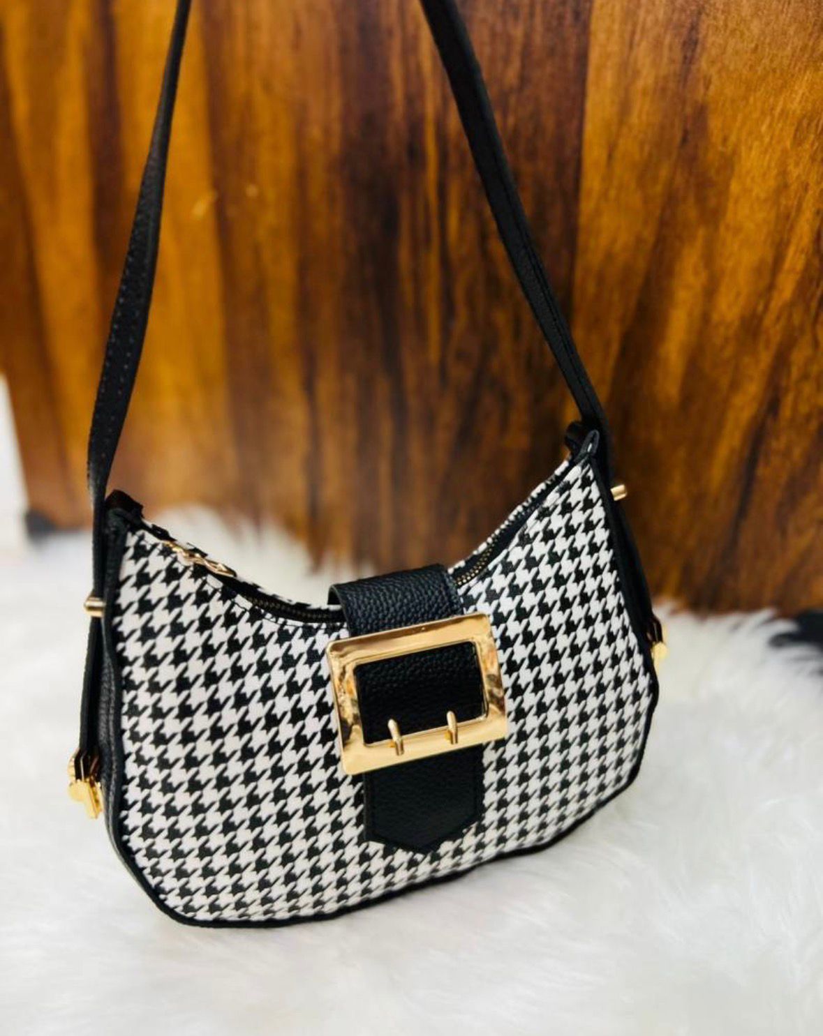 Black and white houndstooth patterned handbag with a gold buckle on a wooden surface.