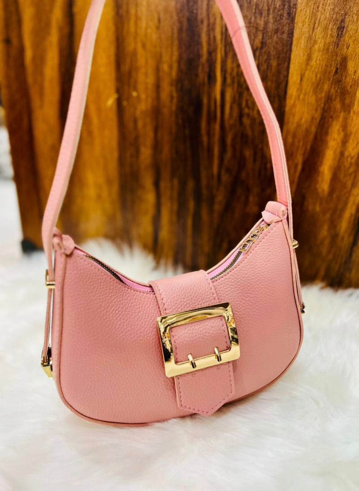 Pink handbag with a gold buckle on a wooden surface