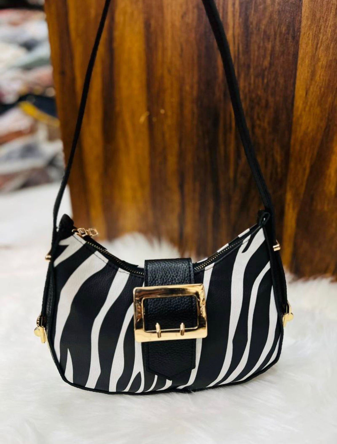 Black and white zebra pattern handbag with gold clasp on a white surface.
