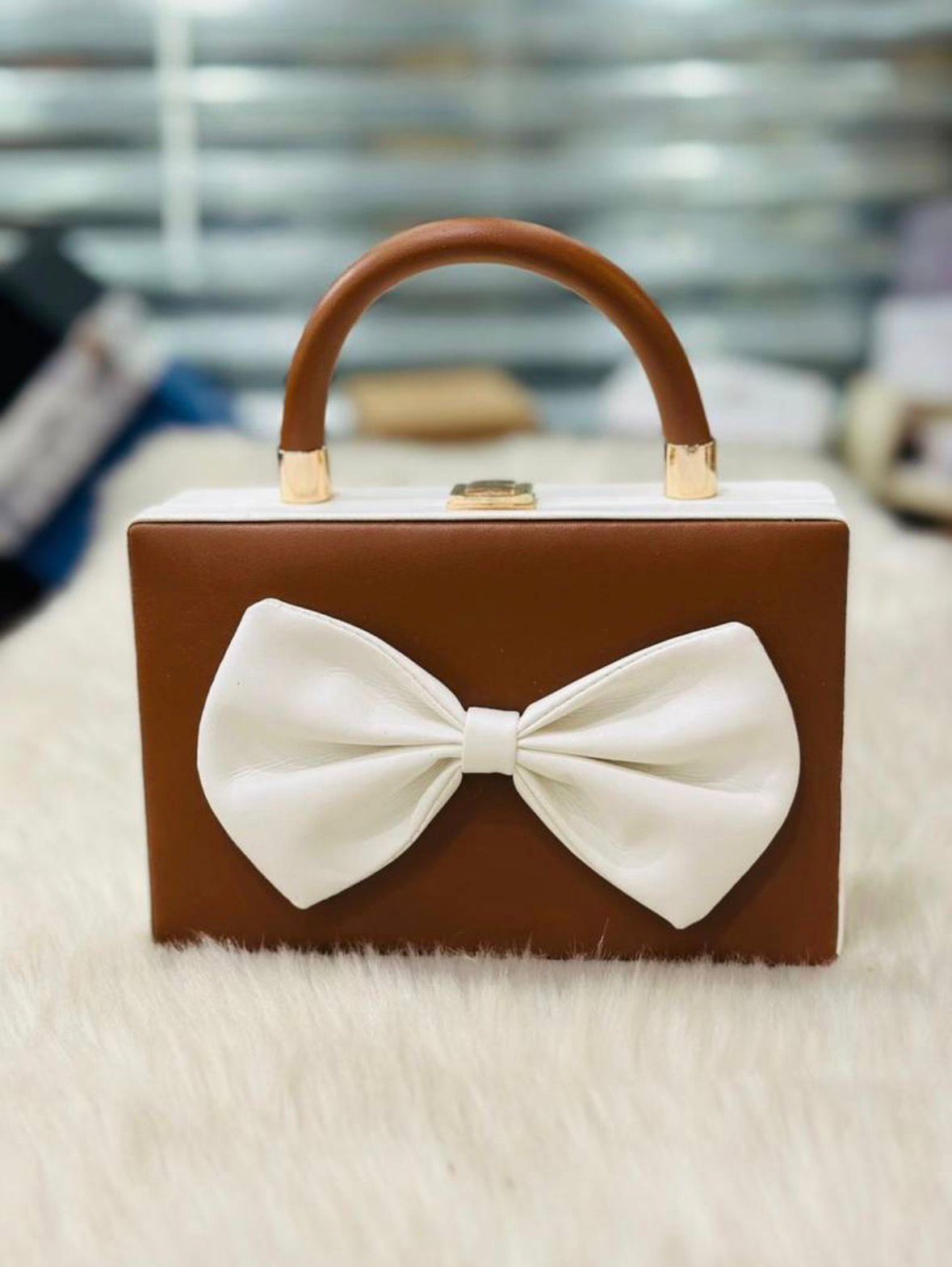 Brown handbag with a large white bow on a fur surface